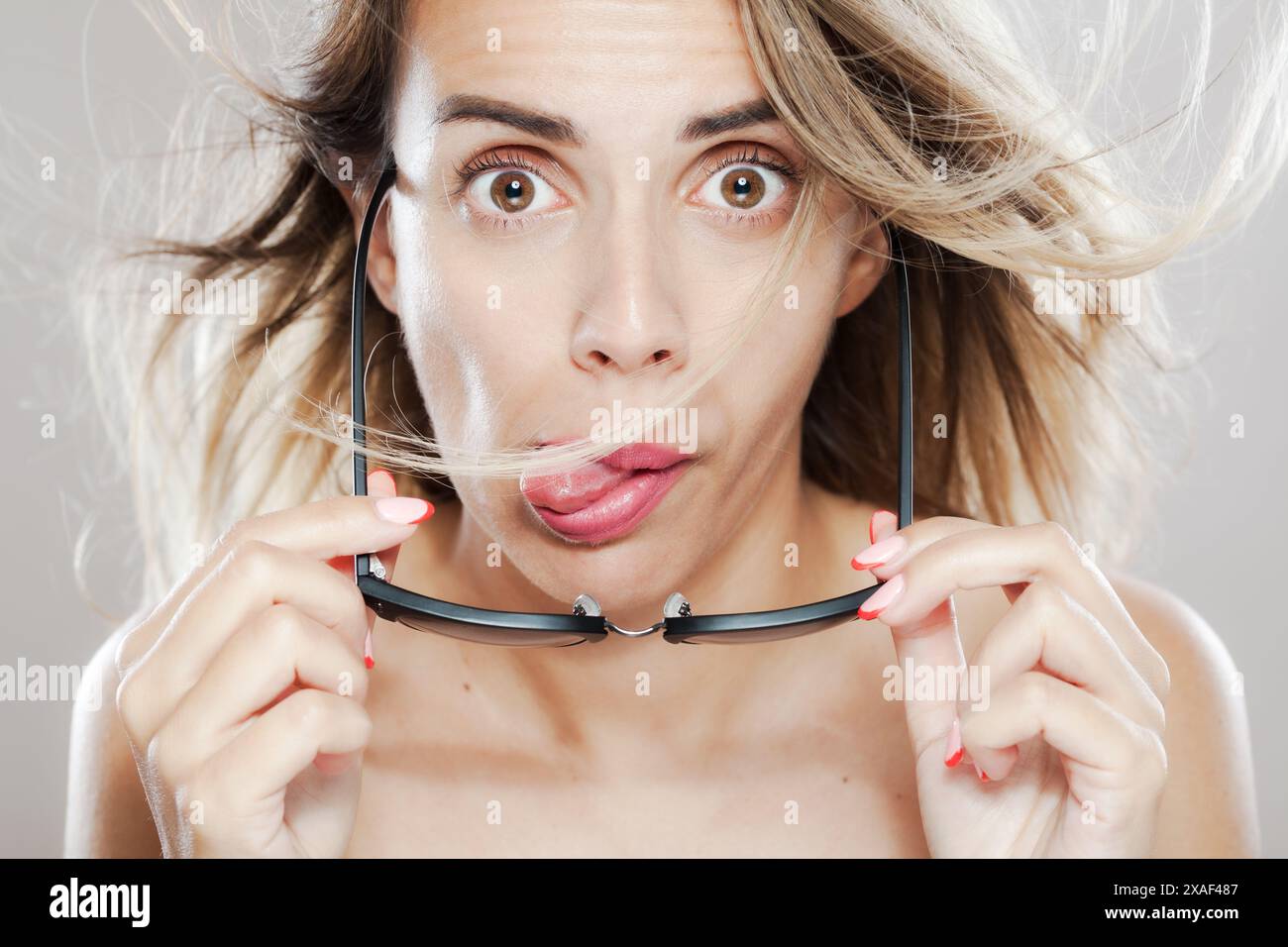 A playful and surprised young woman holding a pair of glasses in front ...