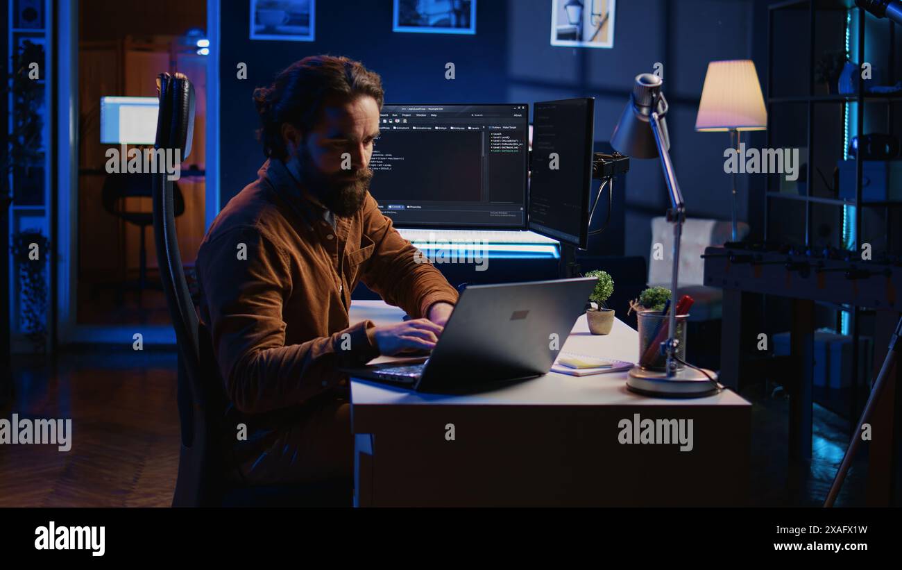 Computer scientist putting headphones on while developing code on PC, making time pass faster during remote job shift. IT admin doing multitasking in home office while listening music, camera B Stock Photo