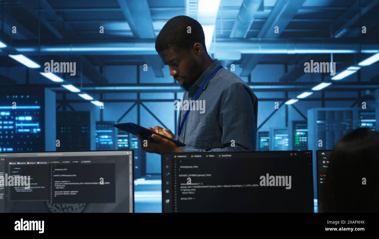Manager uses tablet, supervising team programming servers providing computing resources for different workloads. Inspector using device to oversee engineers in data center mending supercomputers Stock Photo