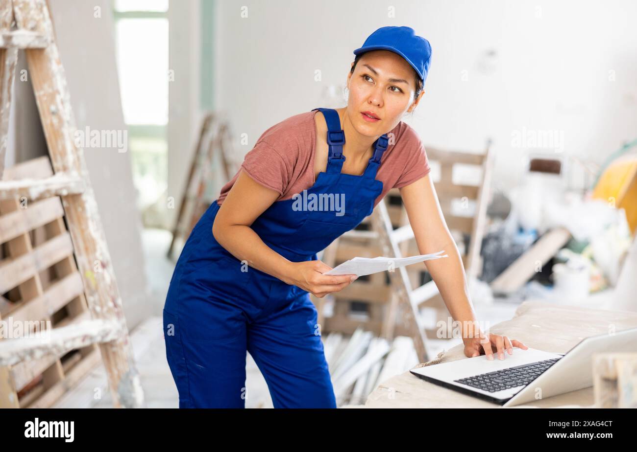 Woman builder checking documentation, using laptop Stock Photo