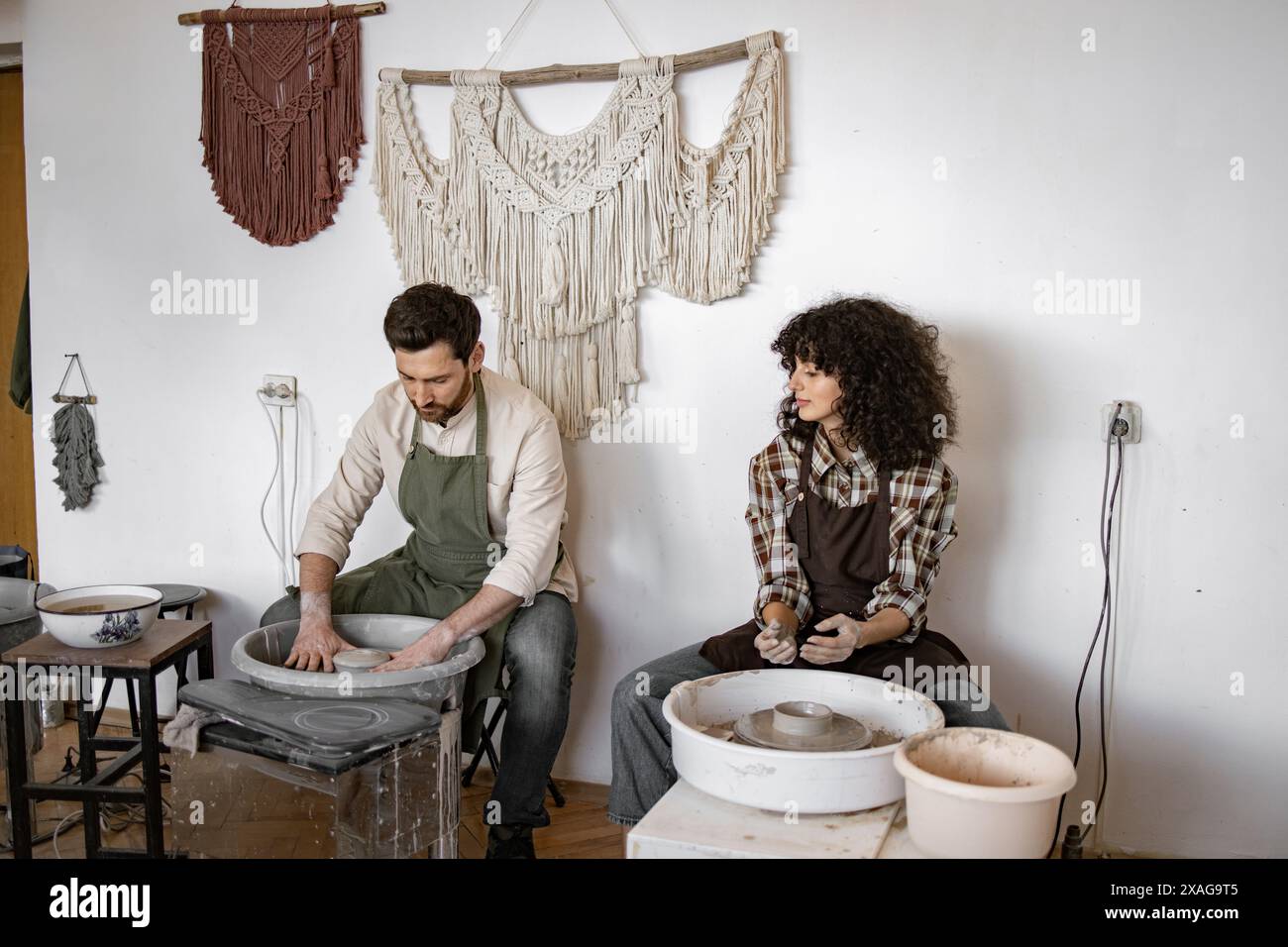 Man and woman potters working together at studio using potter's wheel ...