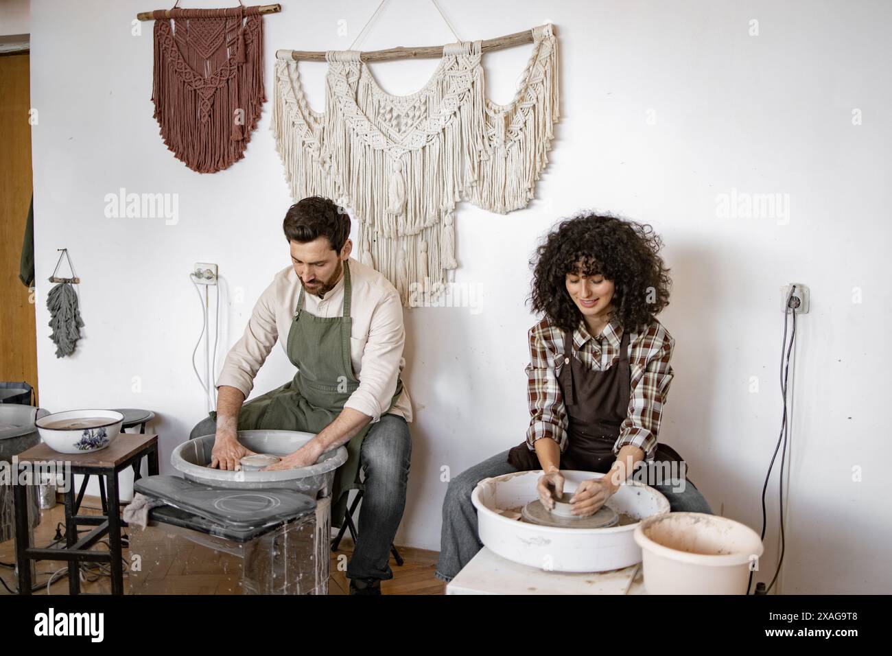 Man and woman creating clay vases on potters wheels in artistic studio ...