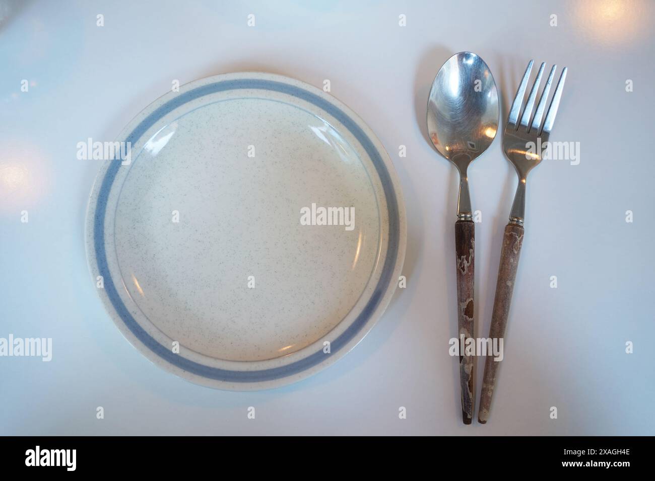 Empty plate with spoon and fork on white table. Top view. Stock Photo