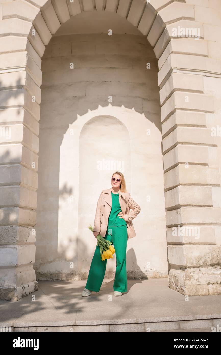 A woman is standing in front of a building with a yellow flower in her ...