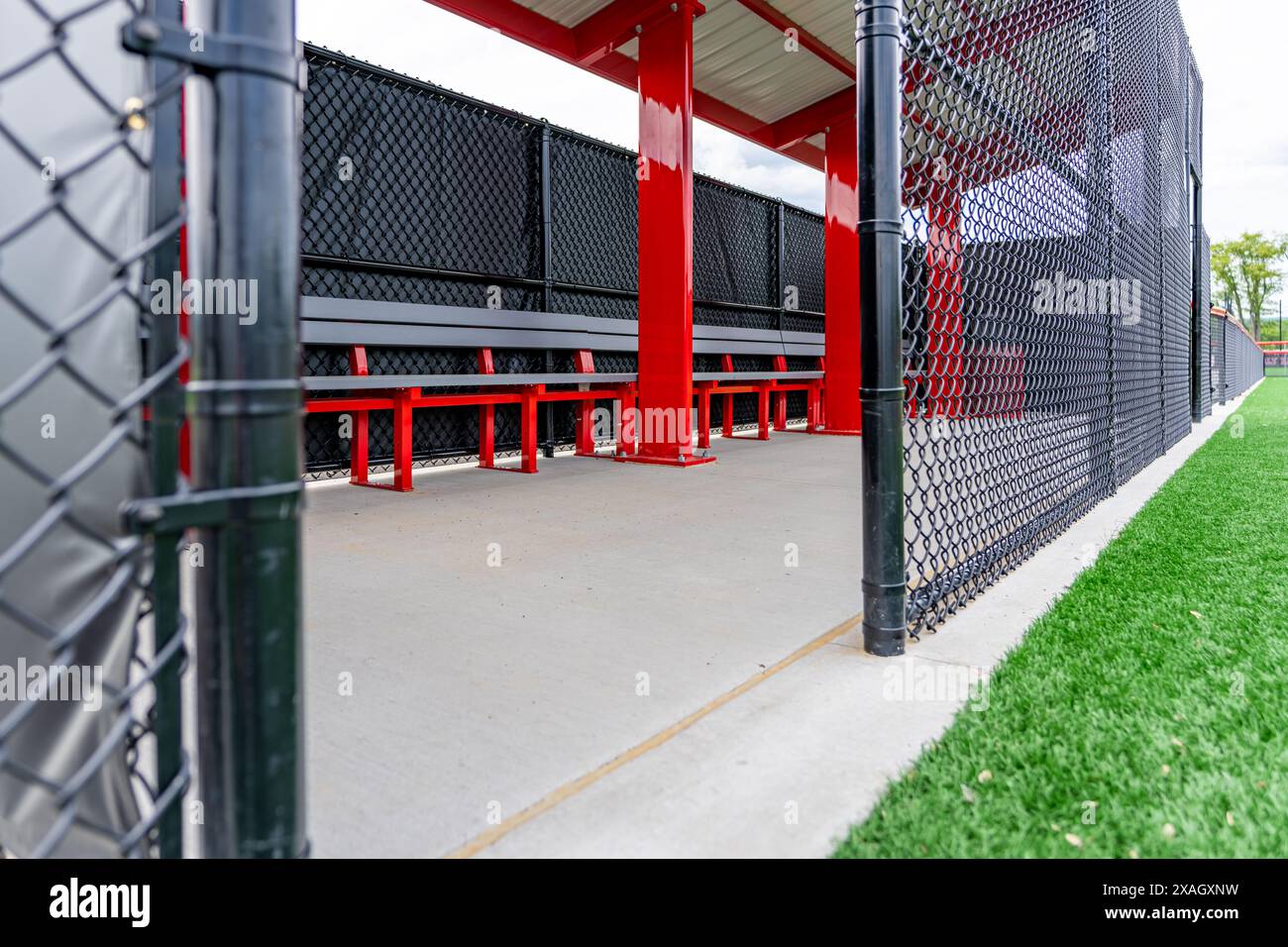 Interior photo of a red softball baseball dugout with roof, concrete