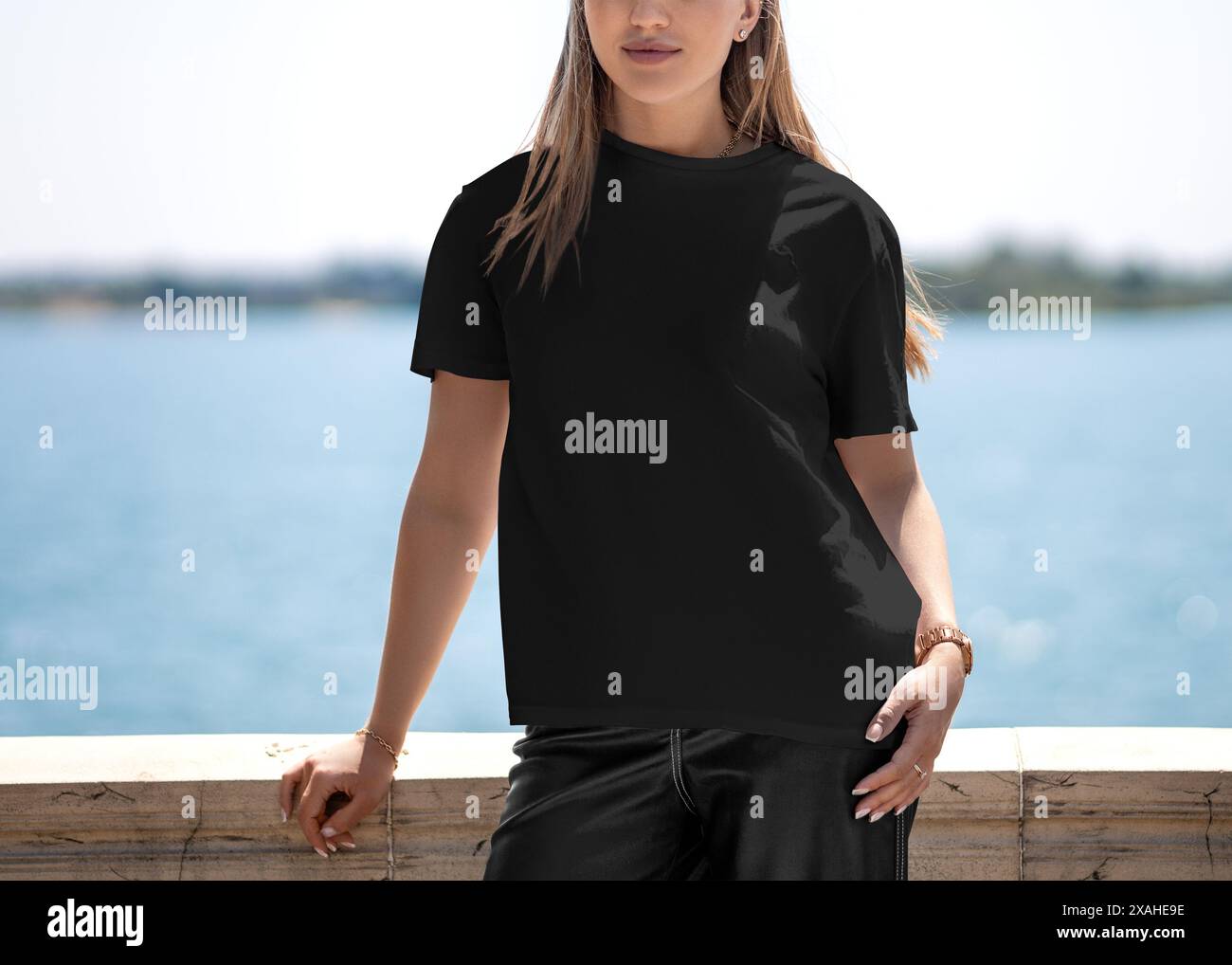Mockup of a black T-shirt on a fair-haired girl in sunny weather on the pier, with a river in the background, front view of a summer shirt. Texture ca Stock Photo
