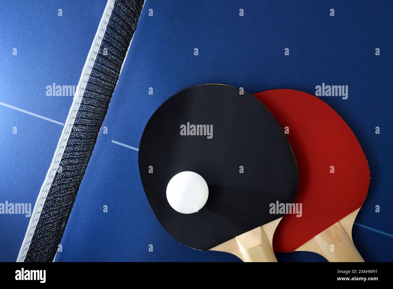 Table tennis paddles and white ball on blue game table with net. Top ...