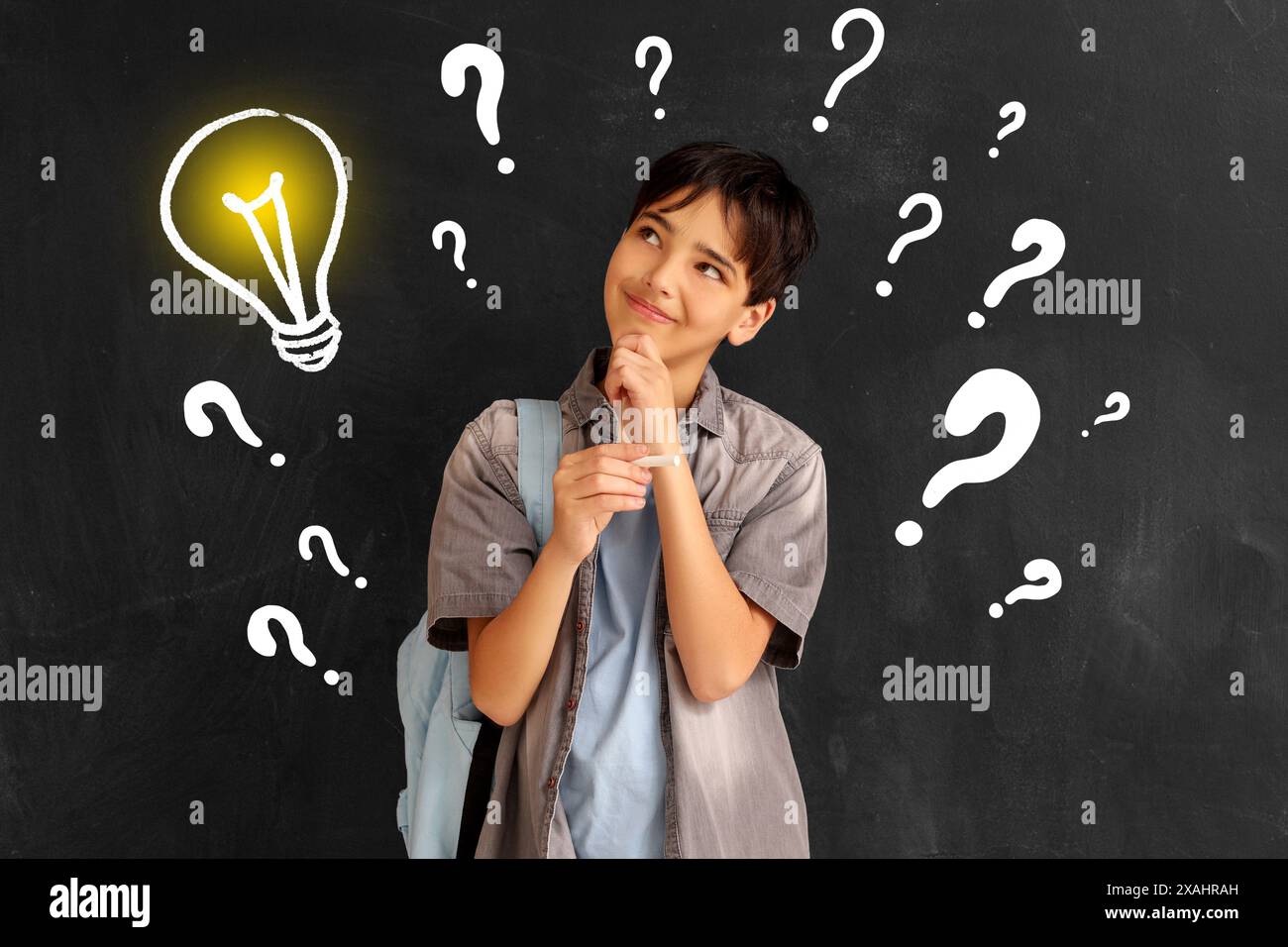 Thoughtful little schoolboy, drawn light bulb and question marks on dark background Stock Photo