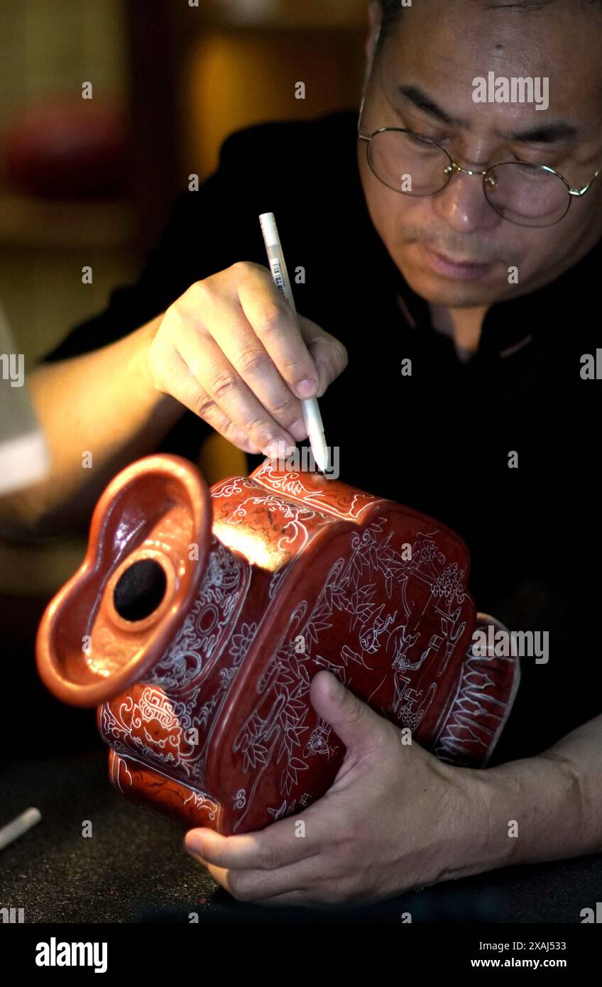 (240607) -- BEIJING, June 7, 2024 (Xinhua) -- Zhu Jiang draws lines on a semi-finished carved lacquer ware at his studio in Beijing, capital of China, June 5, 2024. Carved lacquer, dating back to the Tang Dynasty (618-907), greeted its peak time in Ming and Qing dynasties (1368-1911). Since the founding of the People's Republic of China in 1949, Beijing and Yangzhou have become the two centers for the craft of carved lacquer, which was listed as a national-level intangible cultural heritage in 2006. Carved lacquer differs in its colors, namely red, black or multiple colors. Its making proce Stock Photo