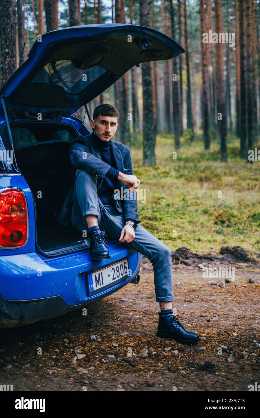 Men with blue Mini Cooper country men and blue umbrella on cloudy day in pine forest. Stock Photo