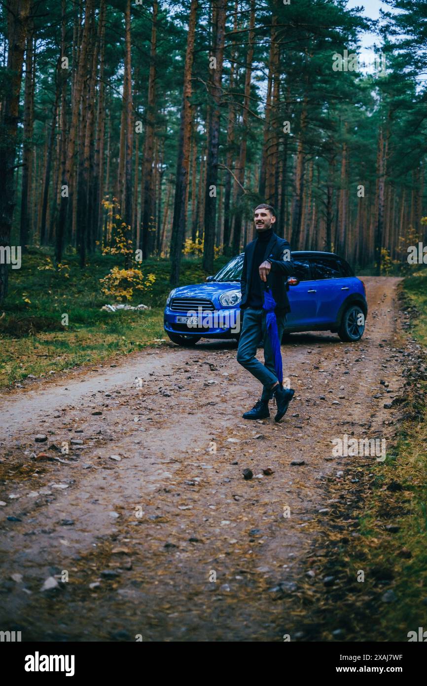 Men with blue Mini Cooper country men and blue umbrella on cloudy day in pine forest. Stock Photo