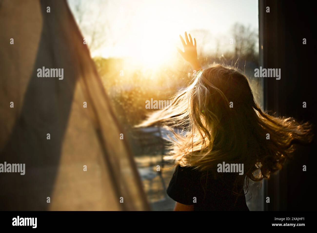 Young girl reaching for sunbeams in bright window Stock Photo