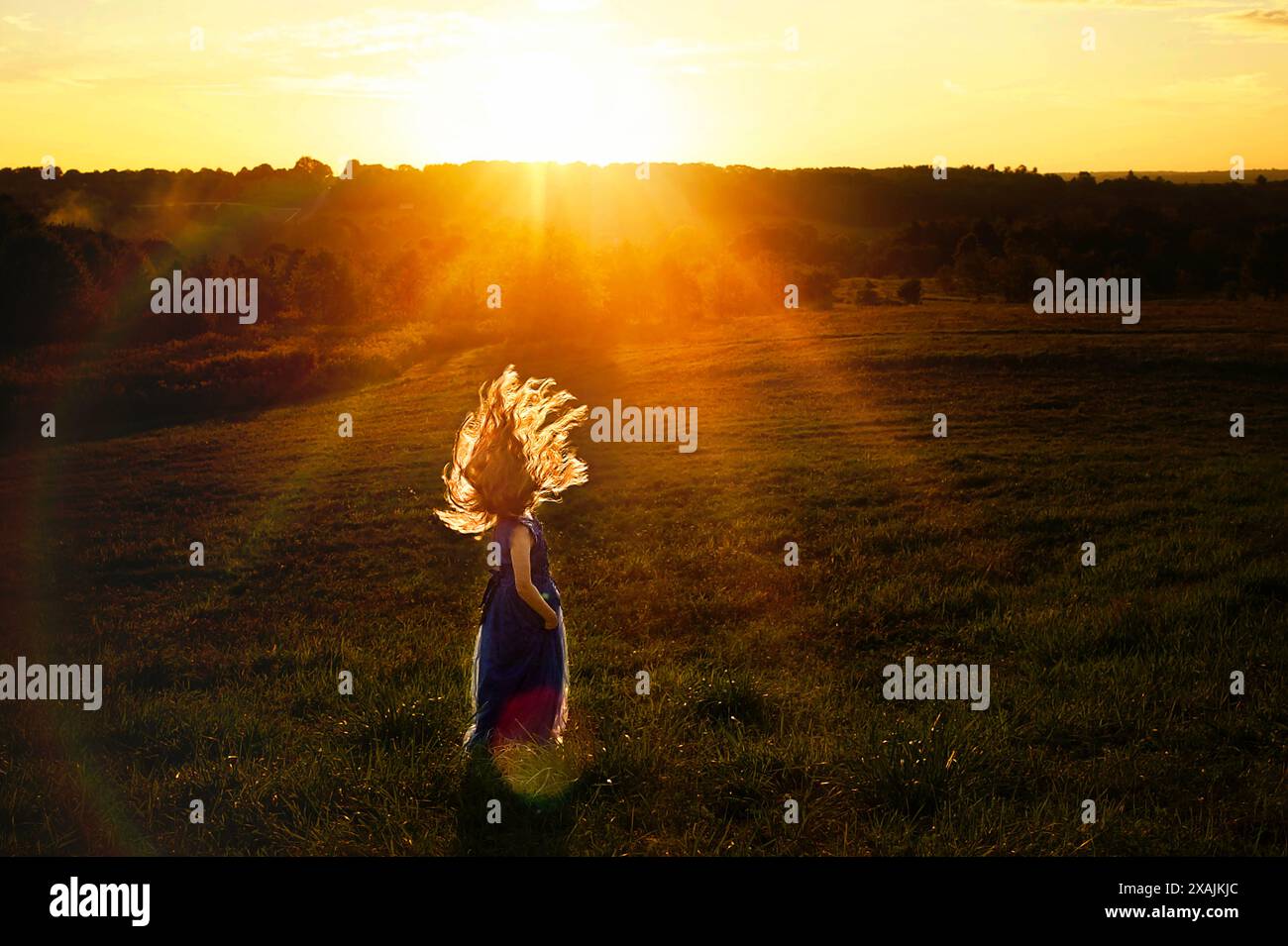 Young girl flipping hair in field at sunset Stock Photo