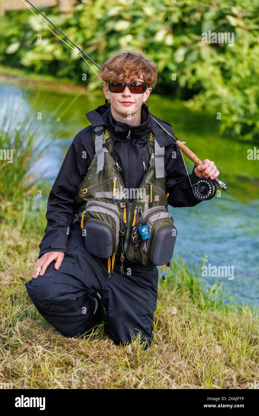 A portrait of a teenage boy in full fishing clothes with his rod over his shoulder fishing on the river in Devon, England. Stock Photo