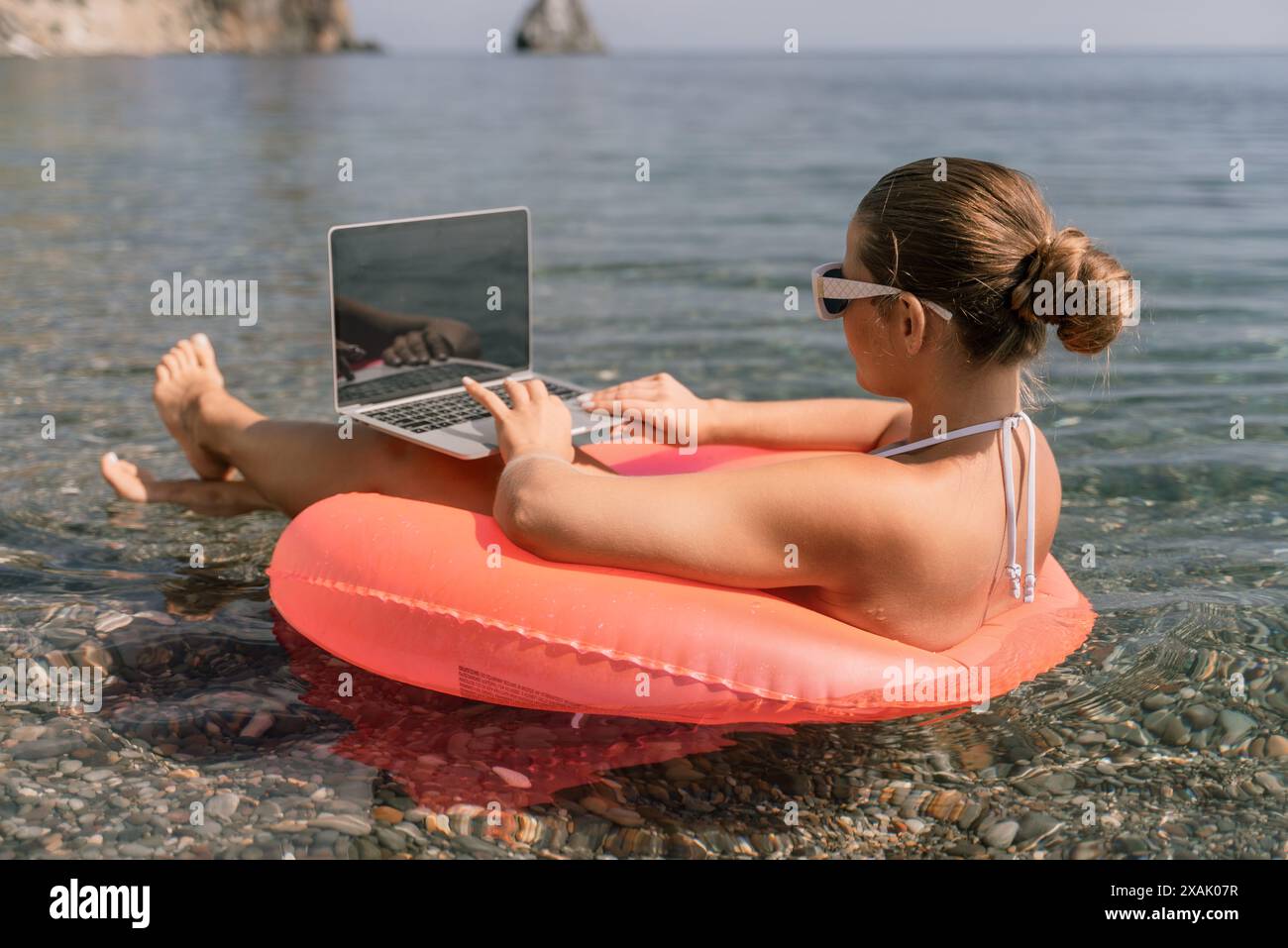 A woman is sitting on a pink inflatable raft in the water, using a ...