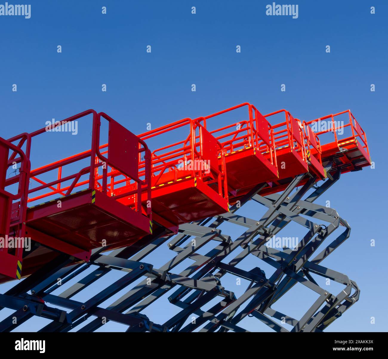 Group of red scissor lifts on a clear blue sky background, low angle