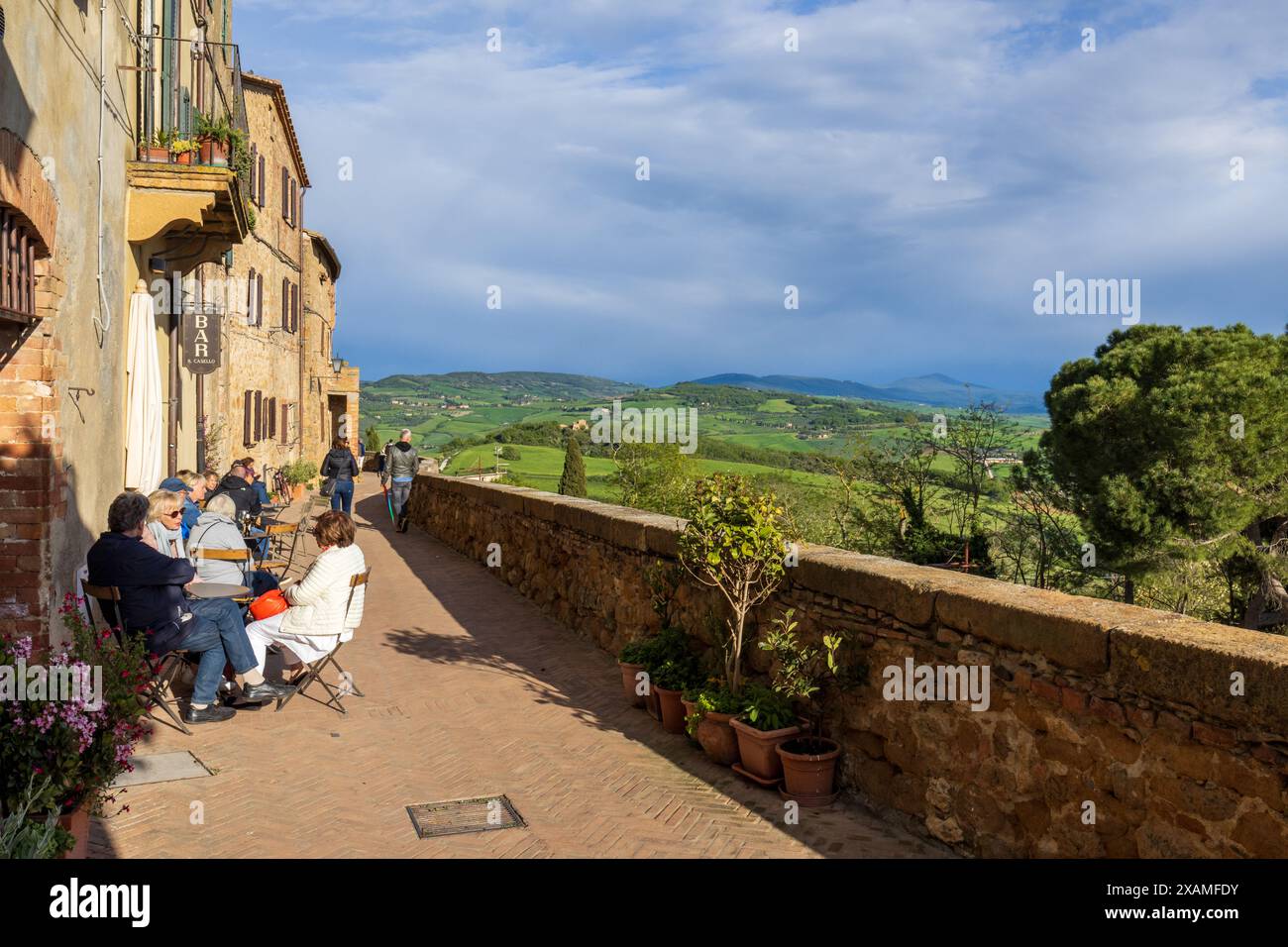A classic scene at the famous viewpoint in Pienza in Tuscany, Italy on a sunny day with cloudy sky, with people sat outside a cafe bar drinking wine. Stock Photo