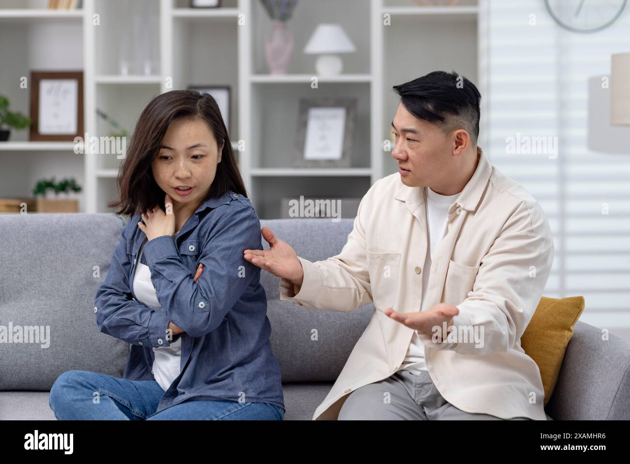 Asian couple having a serious conversation on the couch, capturing emotions of disagreement, concern, and relationship issues in a modern living room setting. Stock Photo