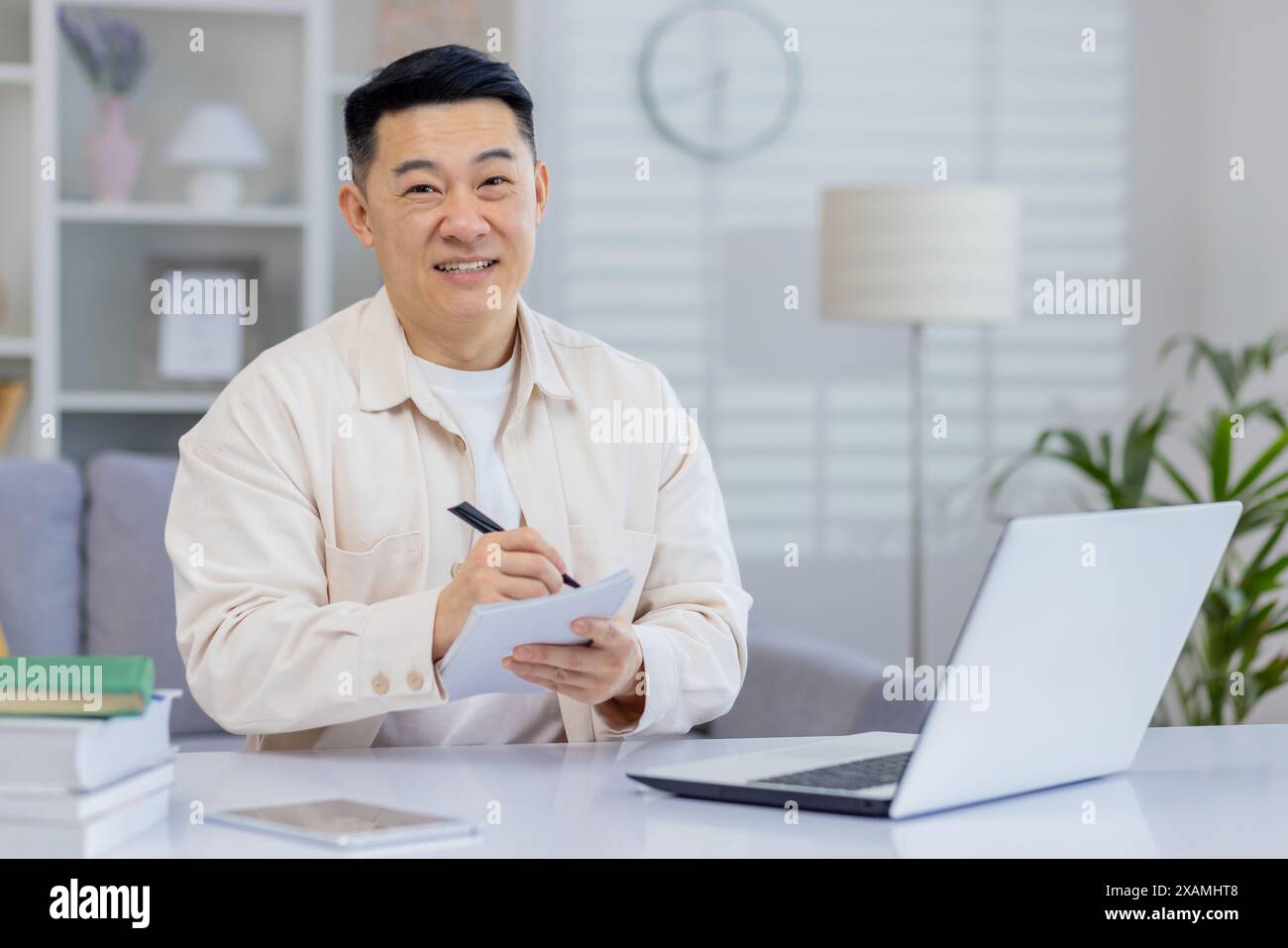 Smiling man working from home taking notes while using a laptop. Relaxed and productive atmosphere. Stock Photo