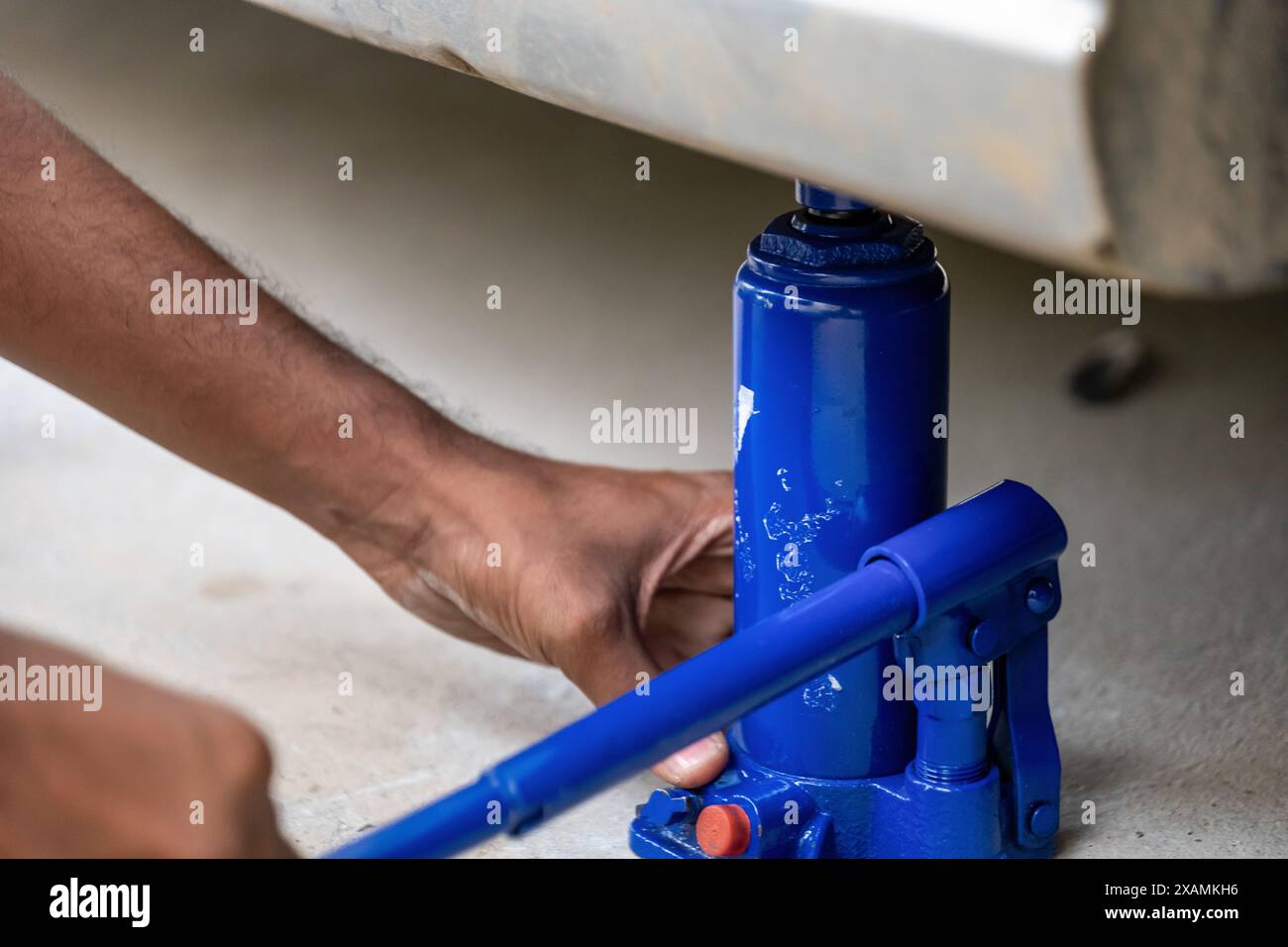 An individual performs car maintenance using a hydraulic bottle jack to