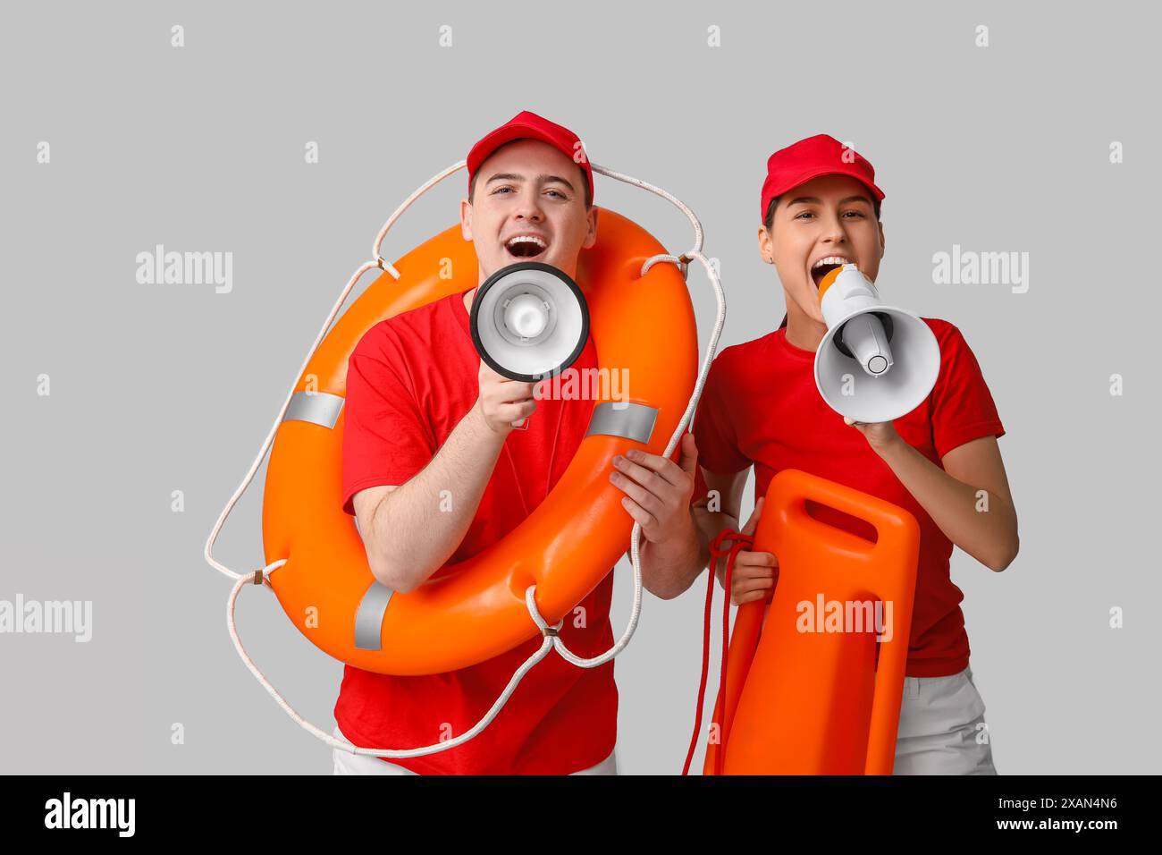 Lifeguards with ring buoy, rescue tube and megaphones on grey background Stock Photo