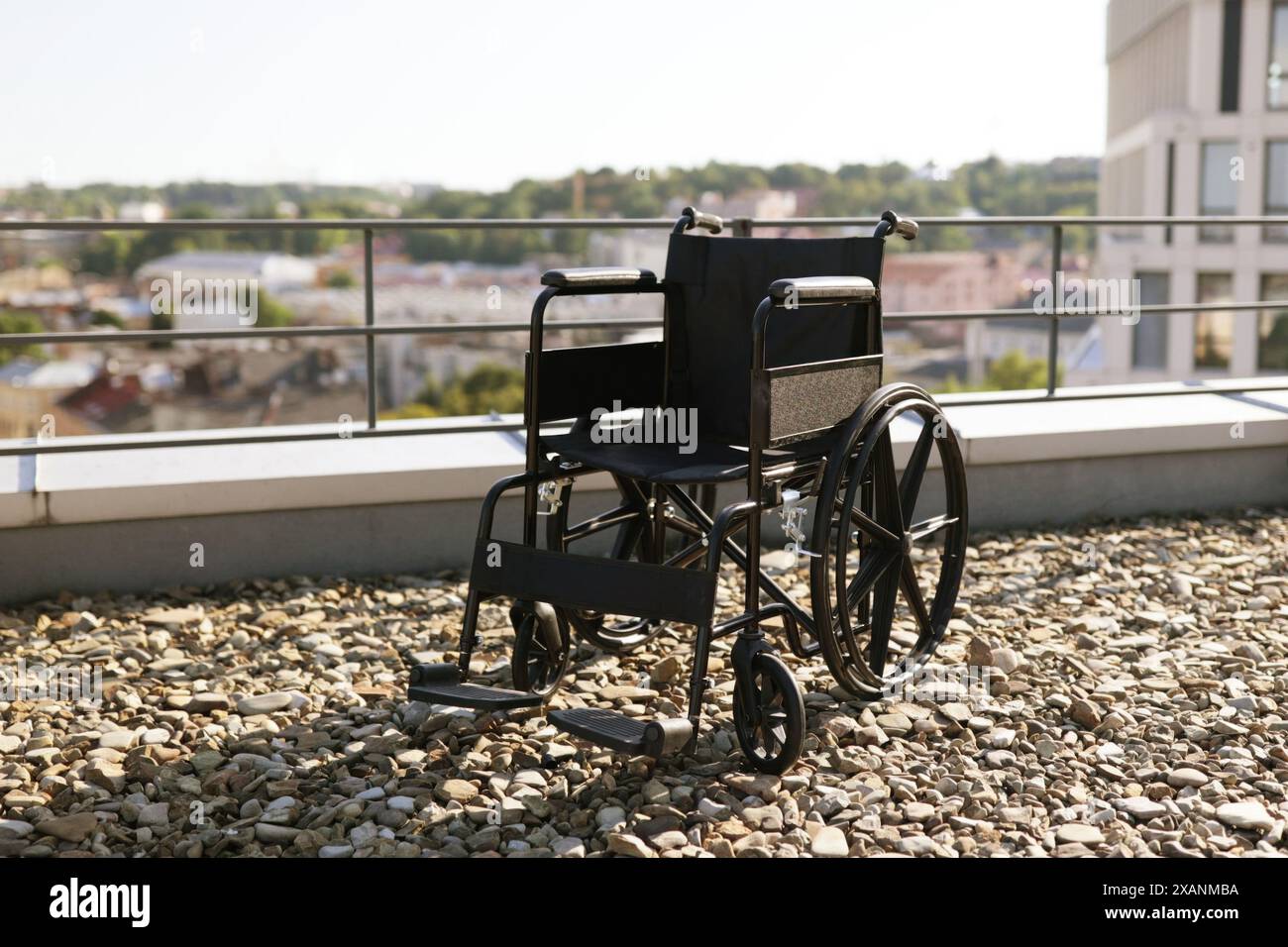 Empty wheelchair on rooftop overlooking cityscape on sunny day Stock Photo