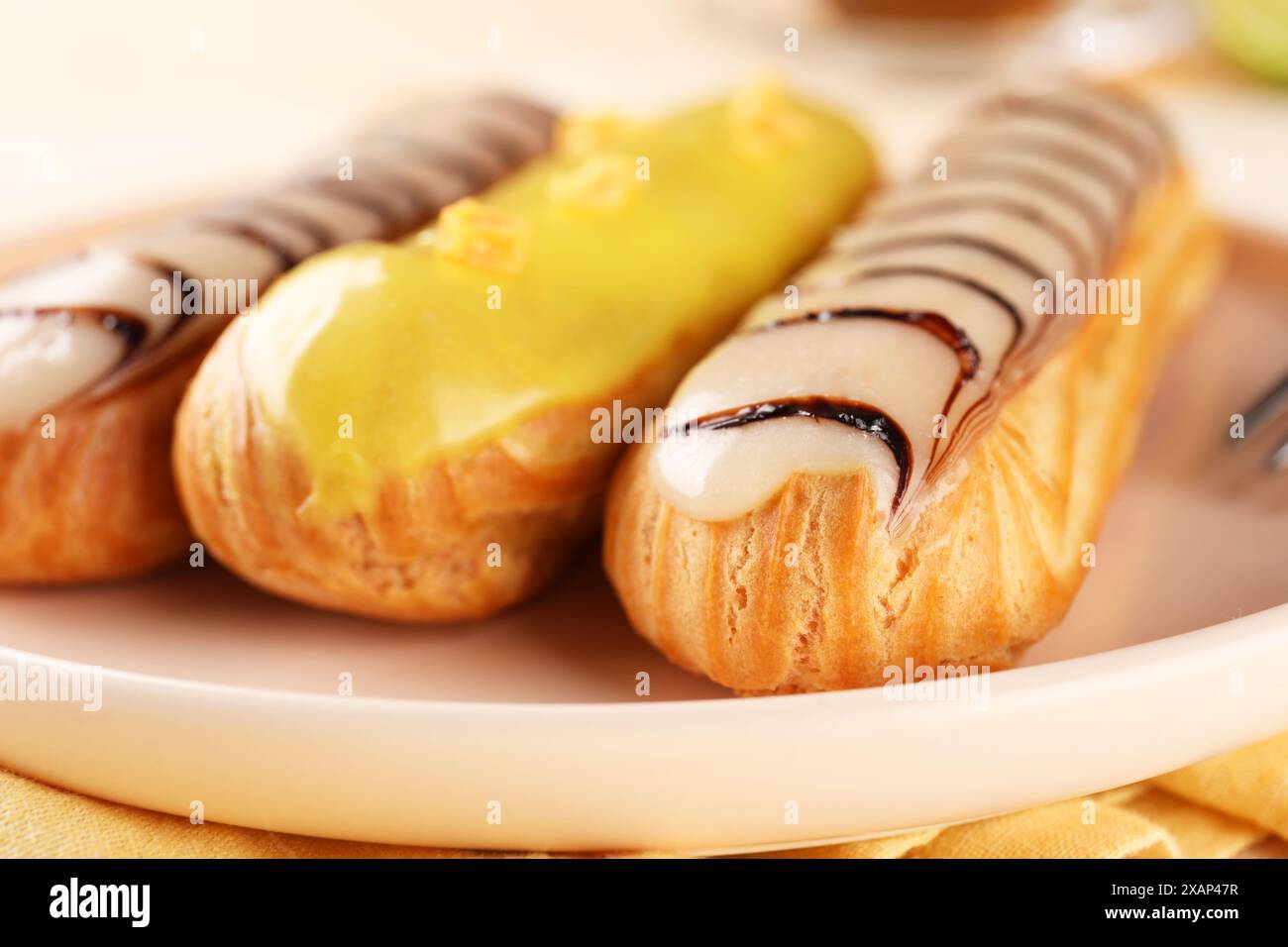 Plate with different tasty glazed eclairs on table, closeup Stock Photo