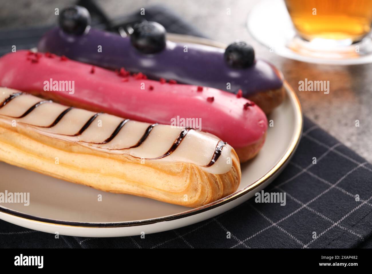 Plate with different tasty glazed eclairs on table, closeup Stock Photo