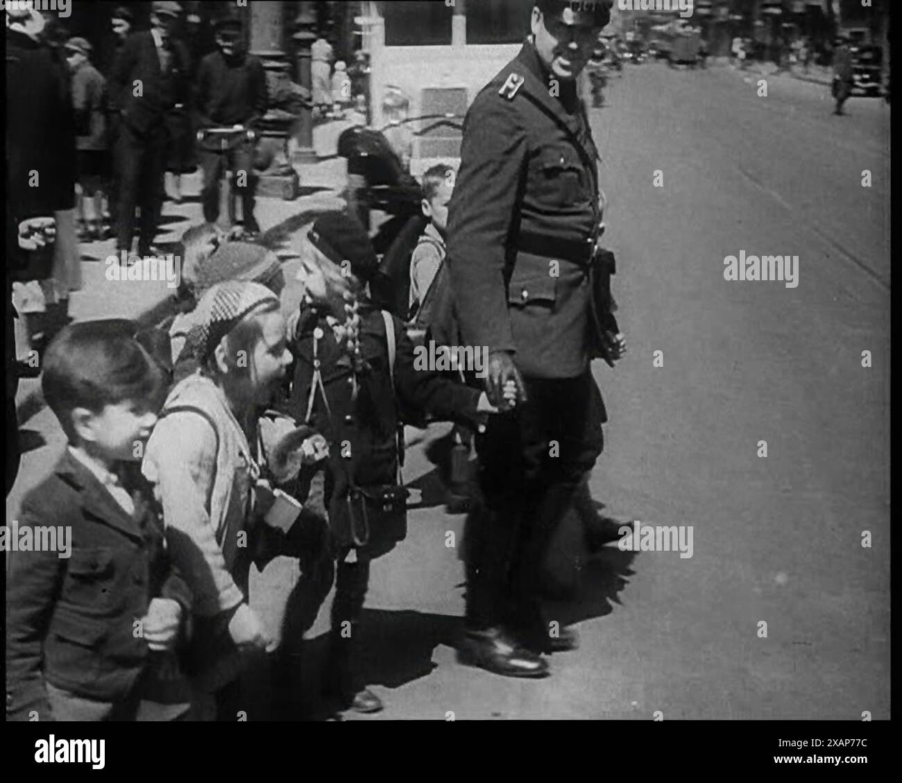 Man in Uniform Helping Young Children Cross the Road, 1933. From &quot;Time To Remember -  The Time Of The Monster&quot;, 1933  (Reel 1); documentary film about events of 1933, rise of Roosevelt and Hitler. Stock Photo