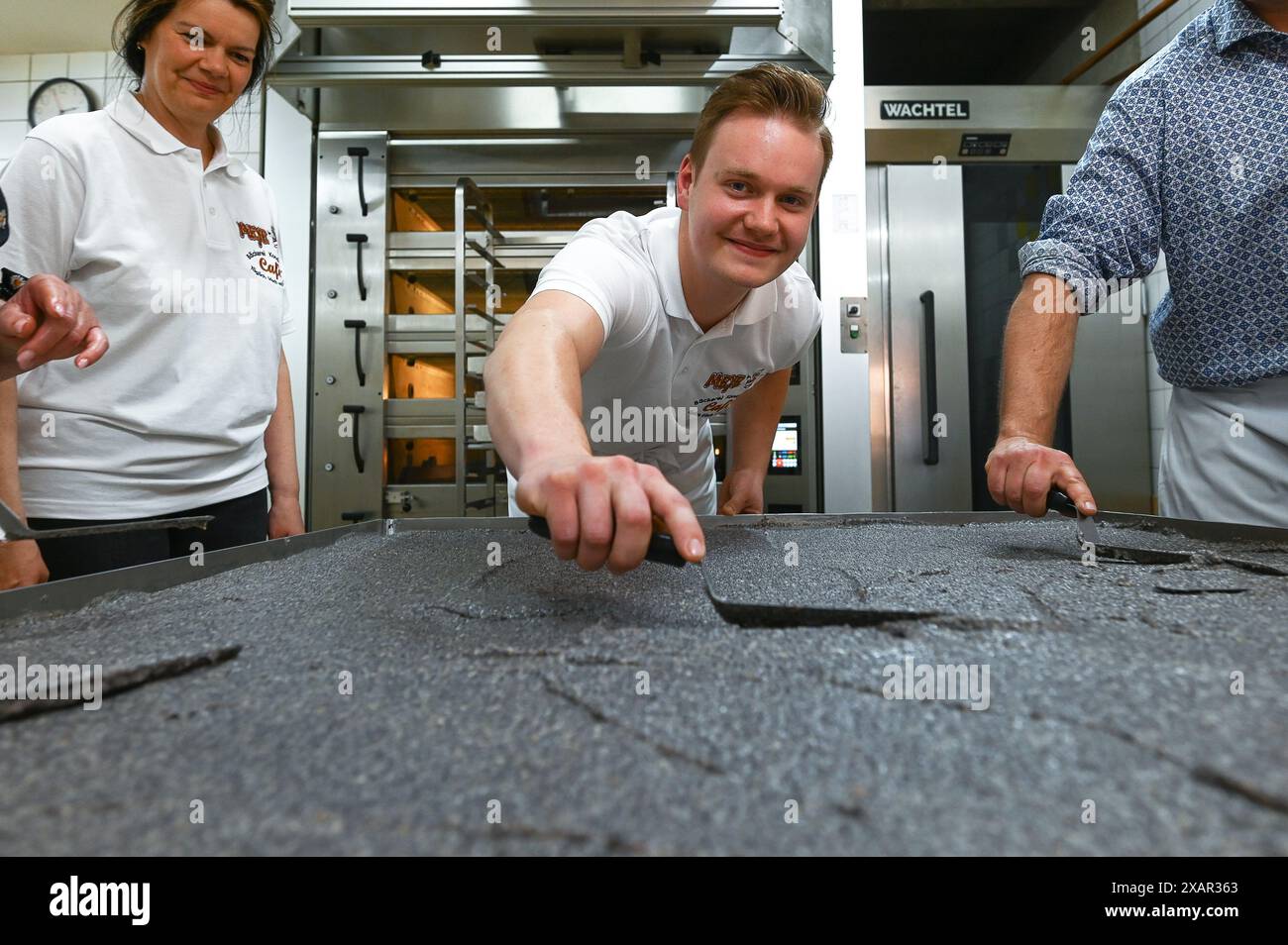 Allstedt, Germany. 08th June, 2024. Master baker Vincent Richter (M) from the Meye bakery smoothes out the poppy seeds on the world's largest poppy seed cake. The record attempt is a campaign by the Saxony-Anhalt Art Foundation to mark the commemorative year '500 years of the Peasants' War and the 500th anniversary of Thomas Müntzer's death' in 2025. Müntzer held his famous sermon at the castle in Allstedt in 1524. Credit: Heiko Rebsch/dpa/Alamy Live News Stock Photo