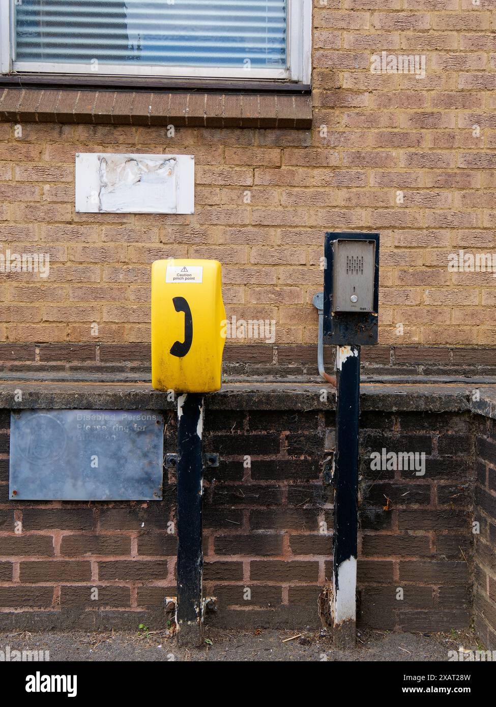 A yellow cabinet of a disabled call-point installed beside a push-button intercom with faded signage outside Faringdon Police Patrol Base Stock Photo