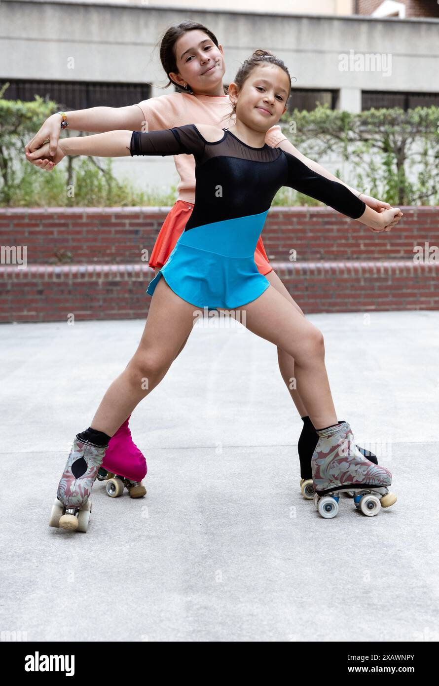 Two young girls in colorful outfits roller skate together in the park ...