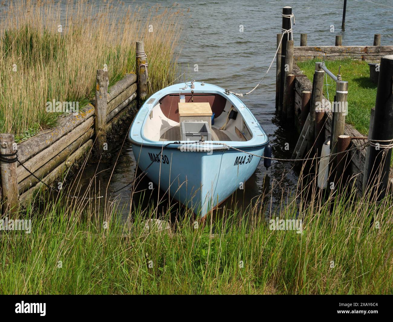 Blue boat in a narrow waterway between wooden jetties on a quiet shoreline, Maasholm, Schleswig-Holstein, Germany Stock Photo