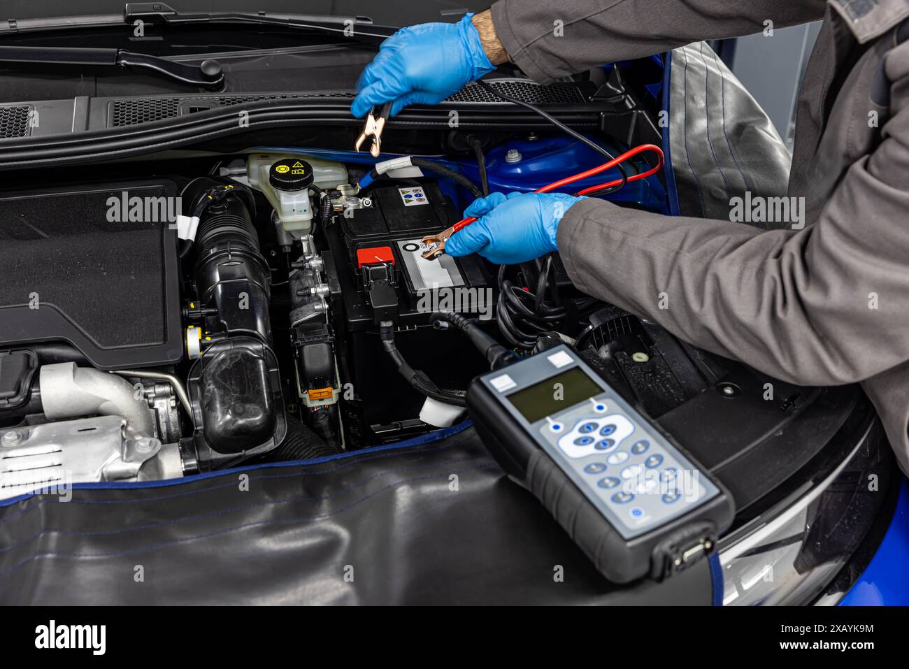 Car master mechanic checking and testing automotive battery with digital electronic battery tester and analyzer in auto vehicle workshop. Stock Photo