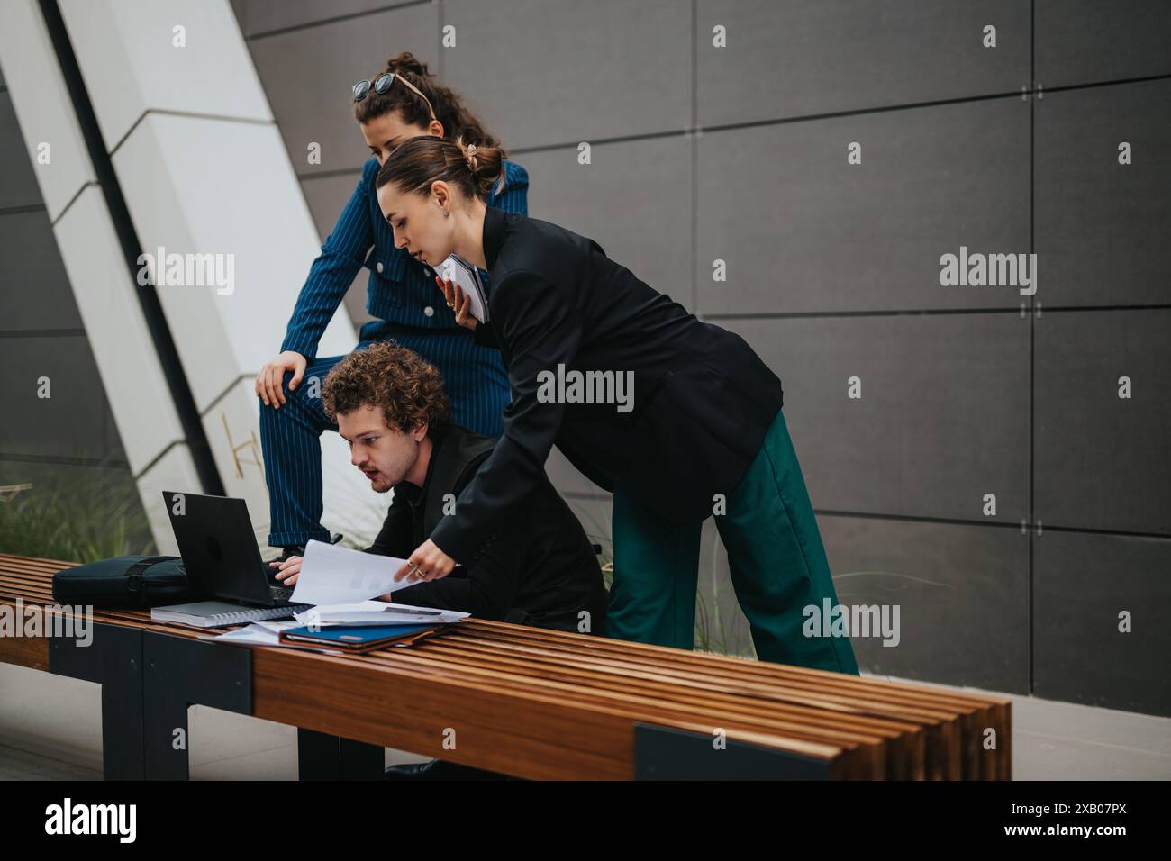 Three young professionals collaborating on a project while looking at a laptop outdoors Stock Photo
