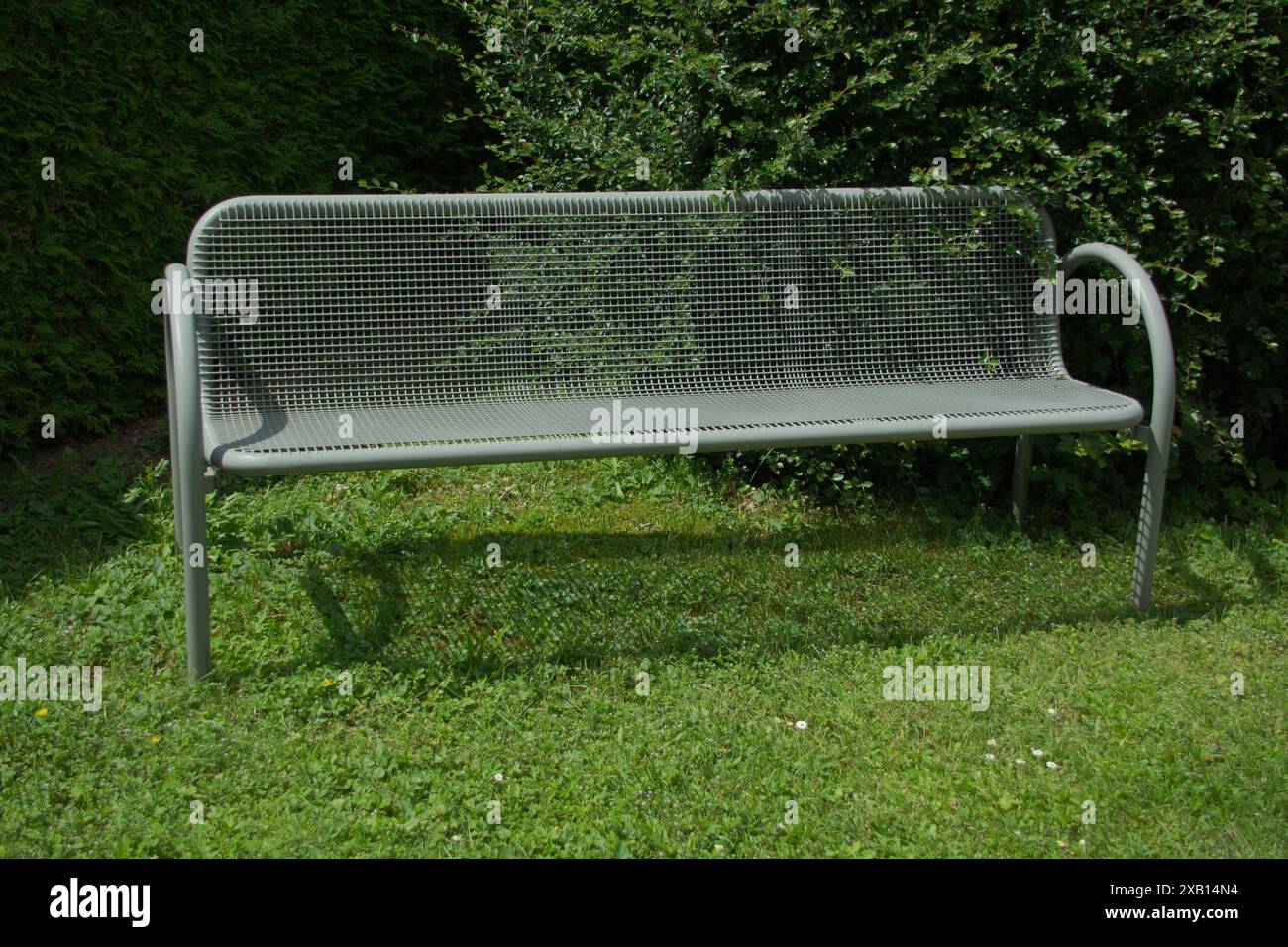 grey metal park bench without people placed in front of a hedge in the ...