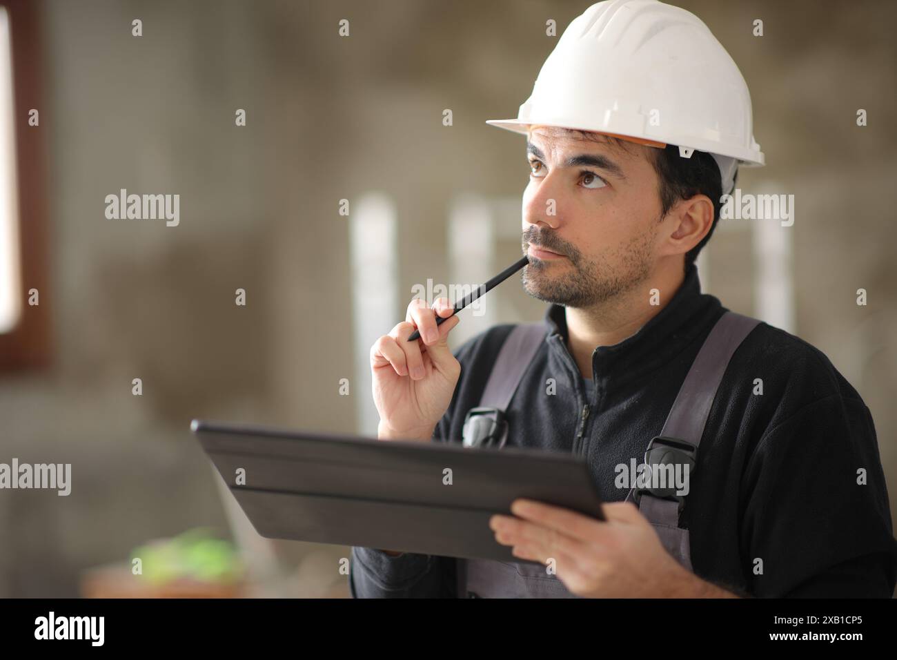 Pensive construction worker holding tablet looking above in a house Stock Photo