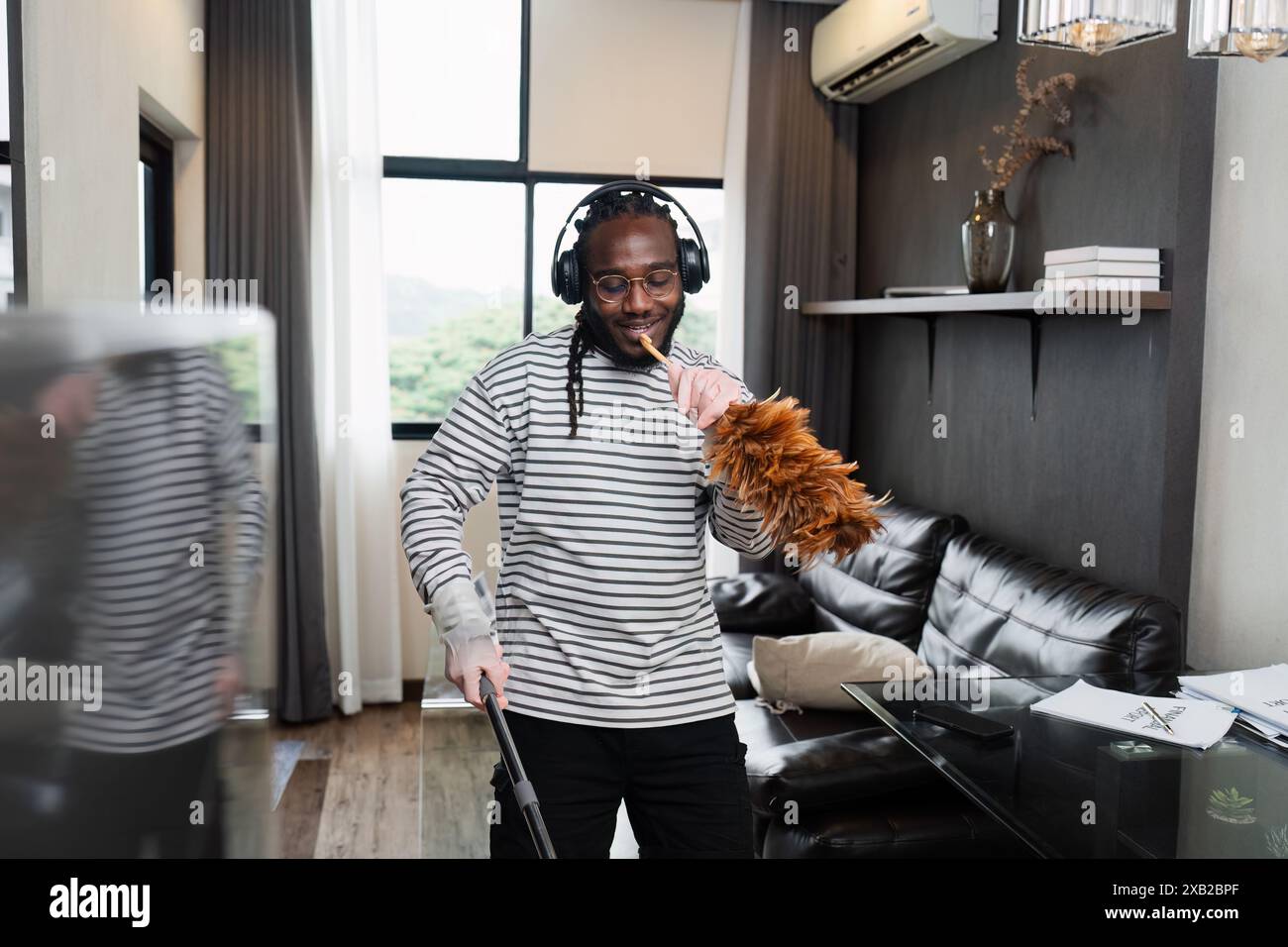Man Enjoying Home Cleaning with Feather Duster and Headphones in Modern ...
