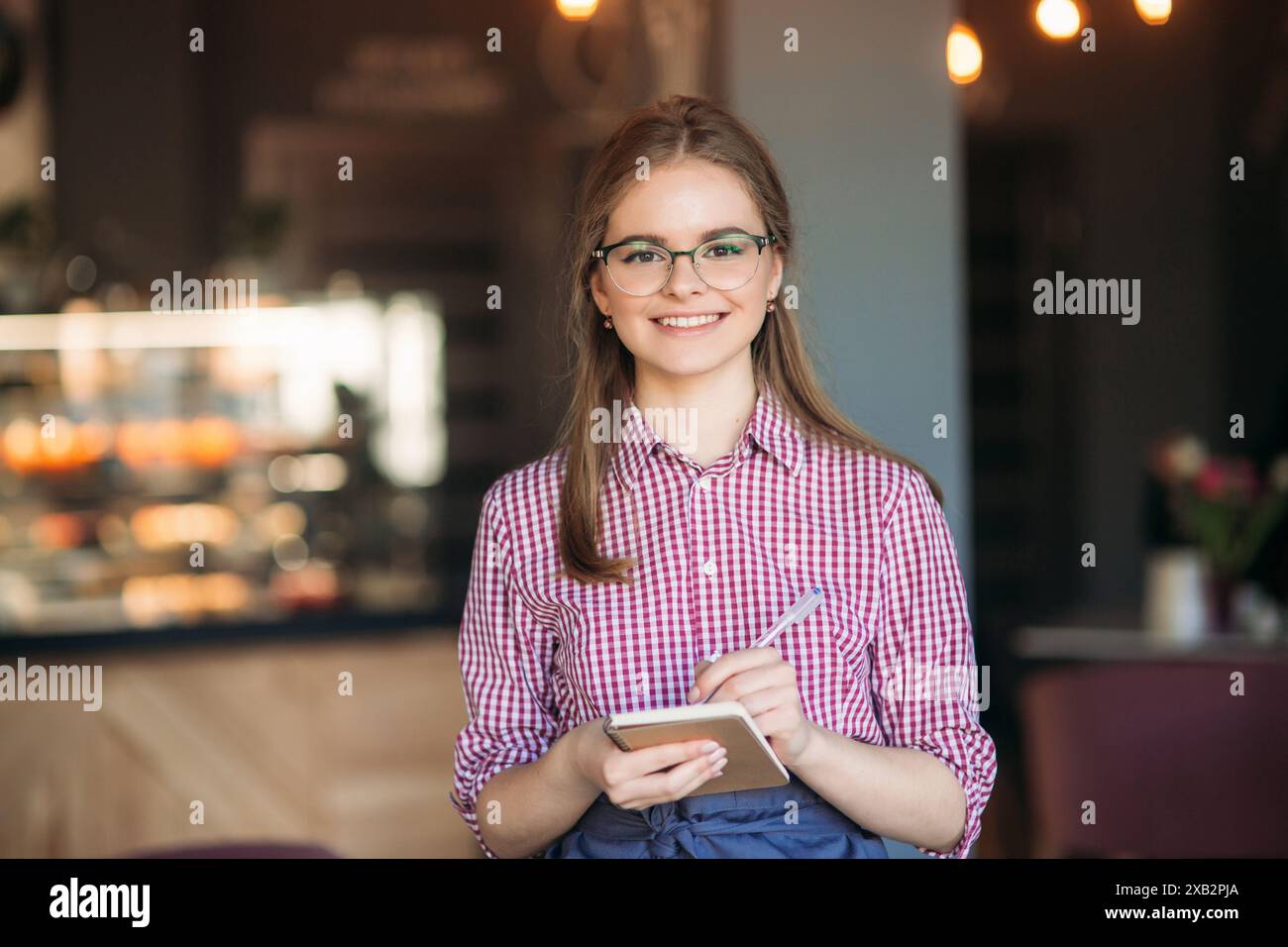 Portrait of a beautiful friendly waitress in glasses with notepapers and pen ready to take your order Stock Photo
