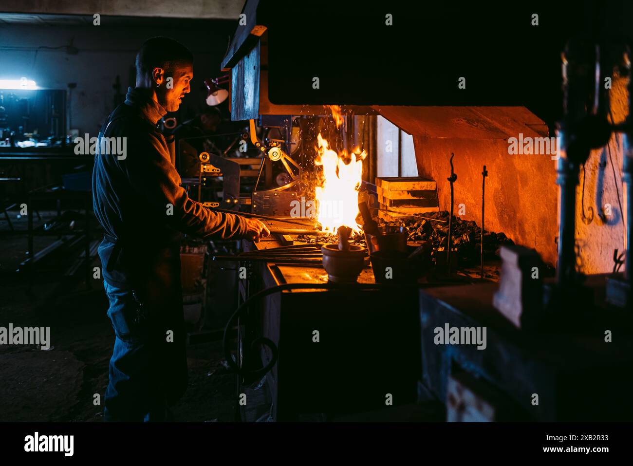 A male blacksmith working with intense fire in his forge, heating up metal surrounded by traditional tools. Stock Photo