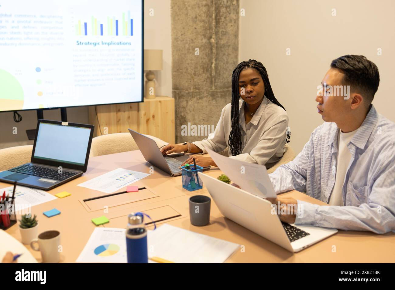 Diverse team collaborates in a modern coworking space, analyzing data on a projector screen Stock Photo
