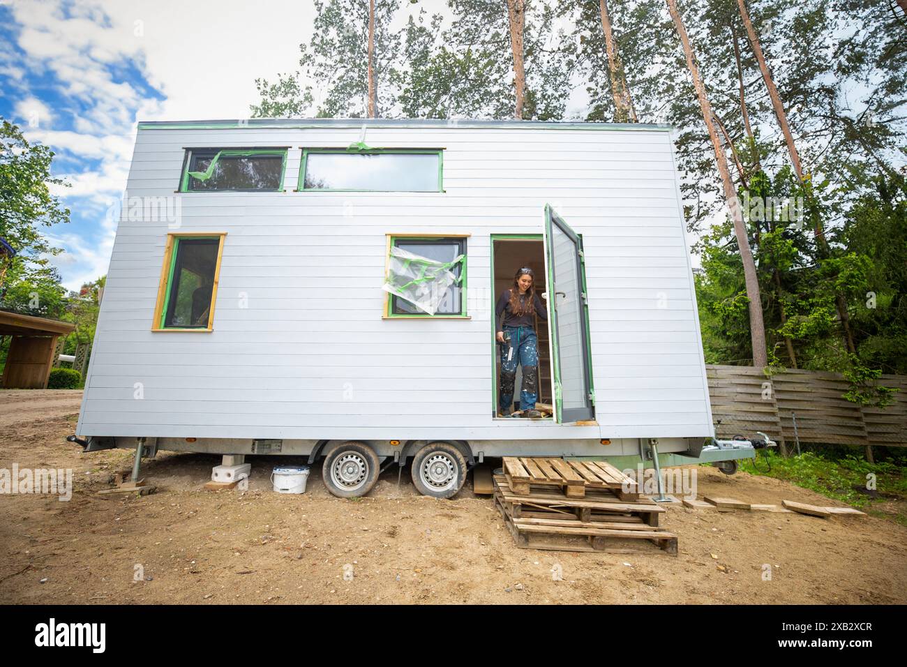 Picture of A young woman stands at the door of a modern tiny house on wheels, set ...