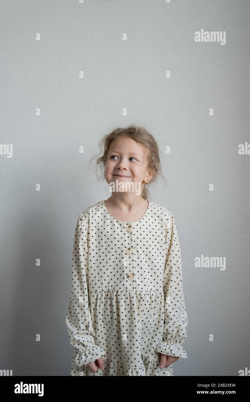 Young girl in a dotted dress smiling and looking away from the camera with a joyful expression. Stock Photo