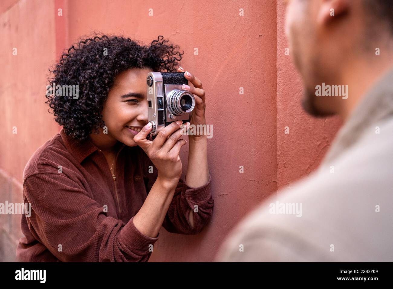 A multiethnic couple enjoys their time in Madrid, Spain. The Hispanic woman is capturing a moment with a vintage camera while the Chinese man stands n Stock Photo