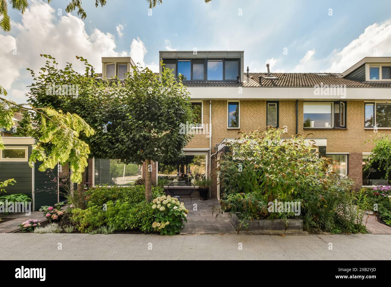 Elegant residence in Rosendael, Amsterdam, featuring a lush, well-maintained front garden with vibrant foliage and a cozy seating area under the shade Stock Photo