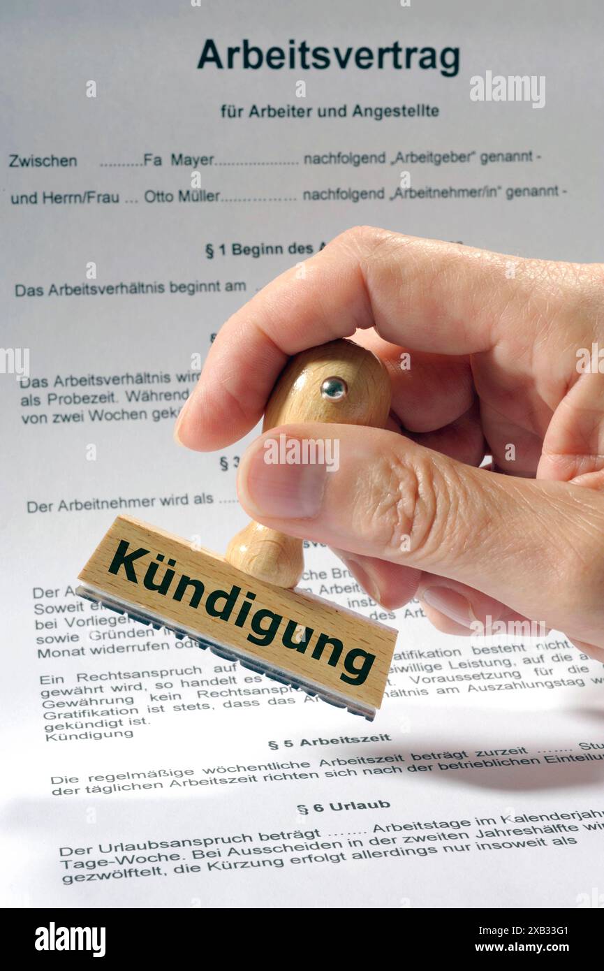 Arbeitsvertrag und Kündigung Eine Hand hält einen Holzstempel mit der Aufschrift Kündigung über einen Arbeitsvertrag *** Employment contract and termi Stock Photo