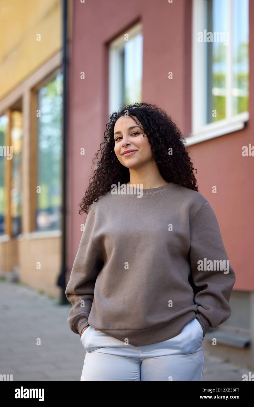 Happy curly haired woman standing with hands in pockets against ...