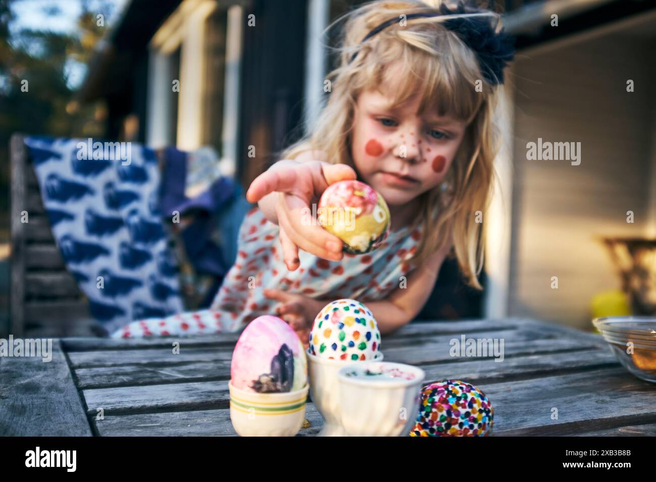 Girl putting colorful Easter eggs in containers on table Stock Photo