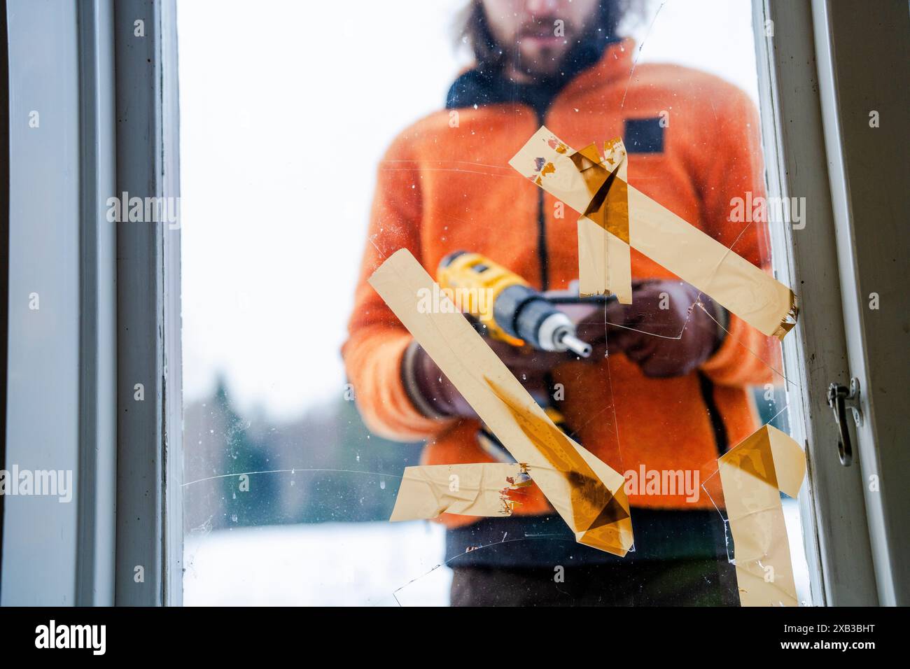 Midsection of man using drill on window glass from outside Stock Photo