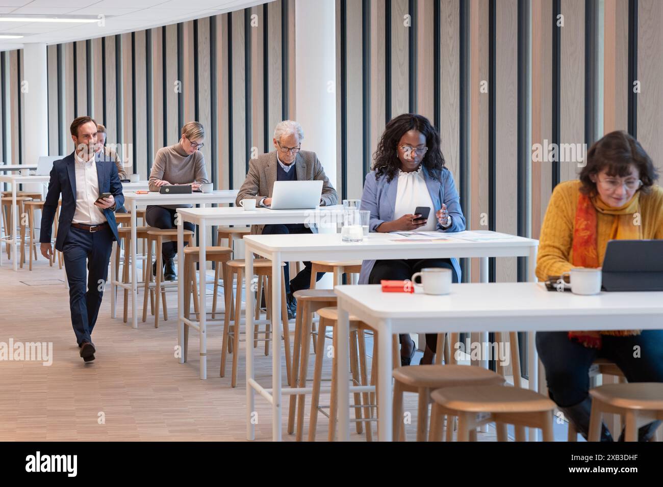 Businessman walking by colleagues sitting at table in office cafeteria Stock Photo